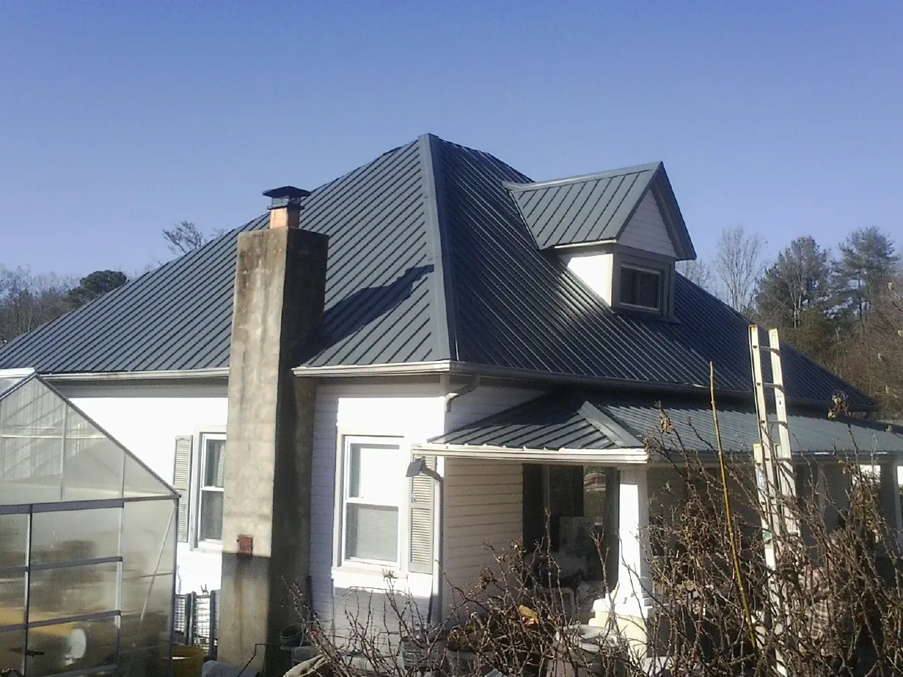 Dark blue standing seam metal roof on a white farmhouse with dormer — Slate & Tile Roof Repair by Roofing Brothers in Yoakum
