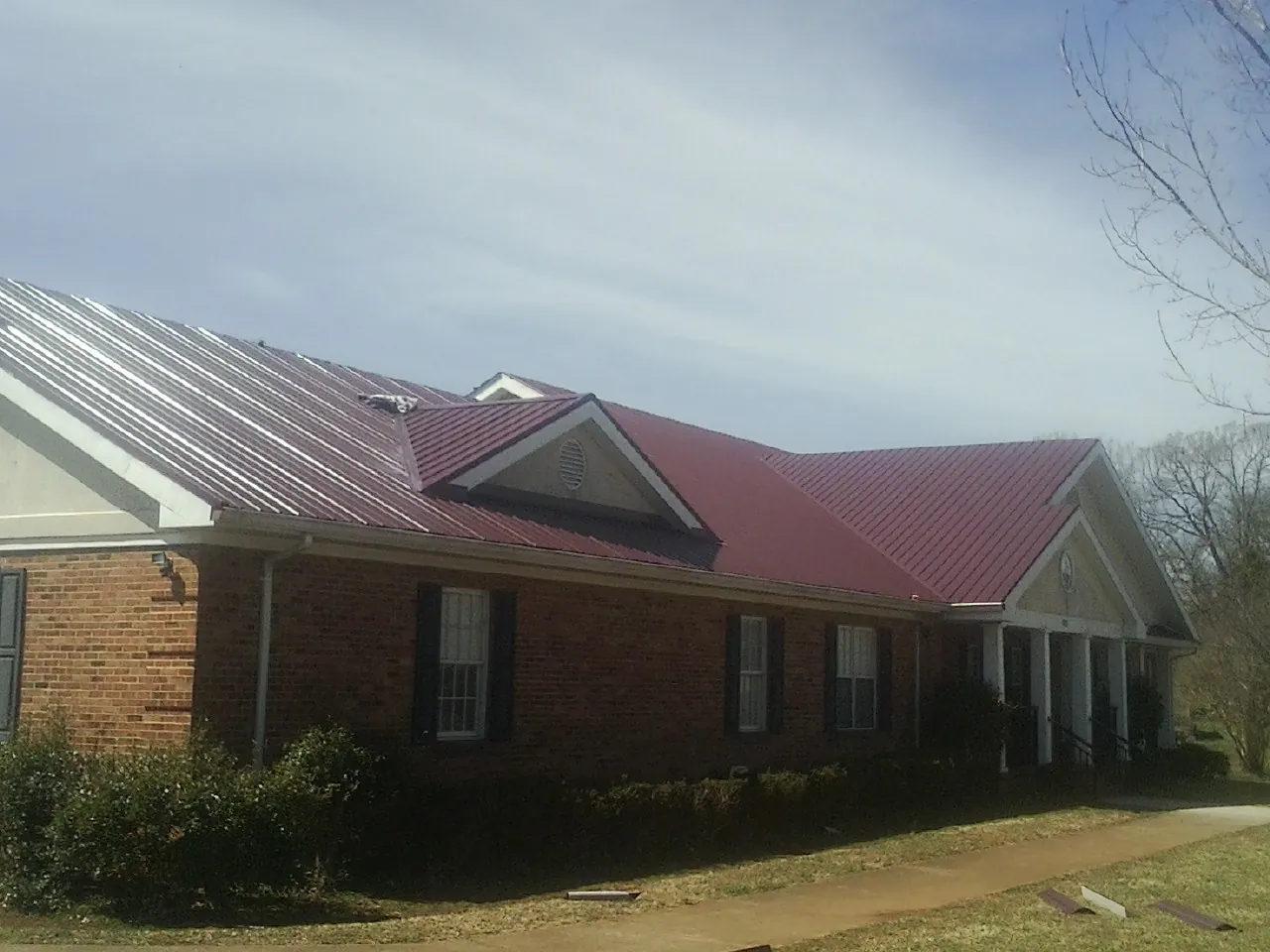 Red metal roof with gabled entries on a long brick building, from a Hail Damage Roof Repair job in Yoakum