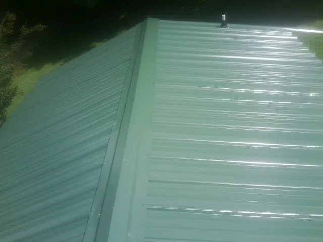 New green metal panels meeting at the ridge of a roof — Flat Roof Repair work by our crew in Yoakum