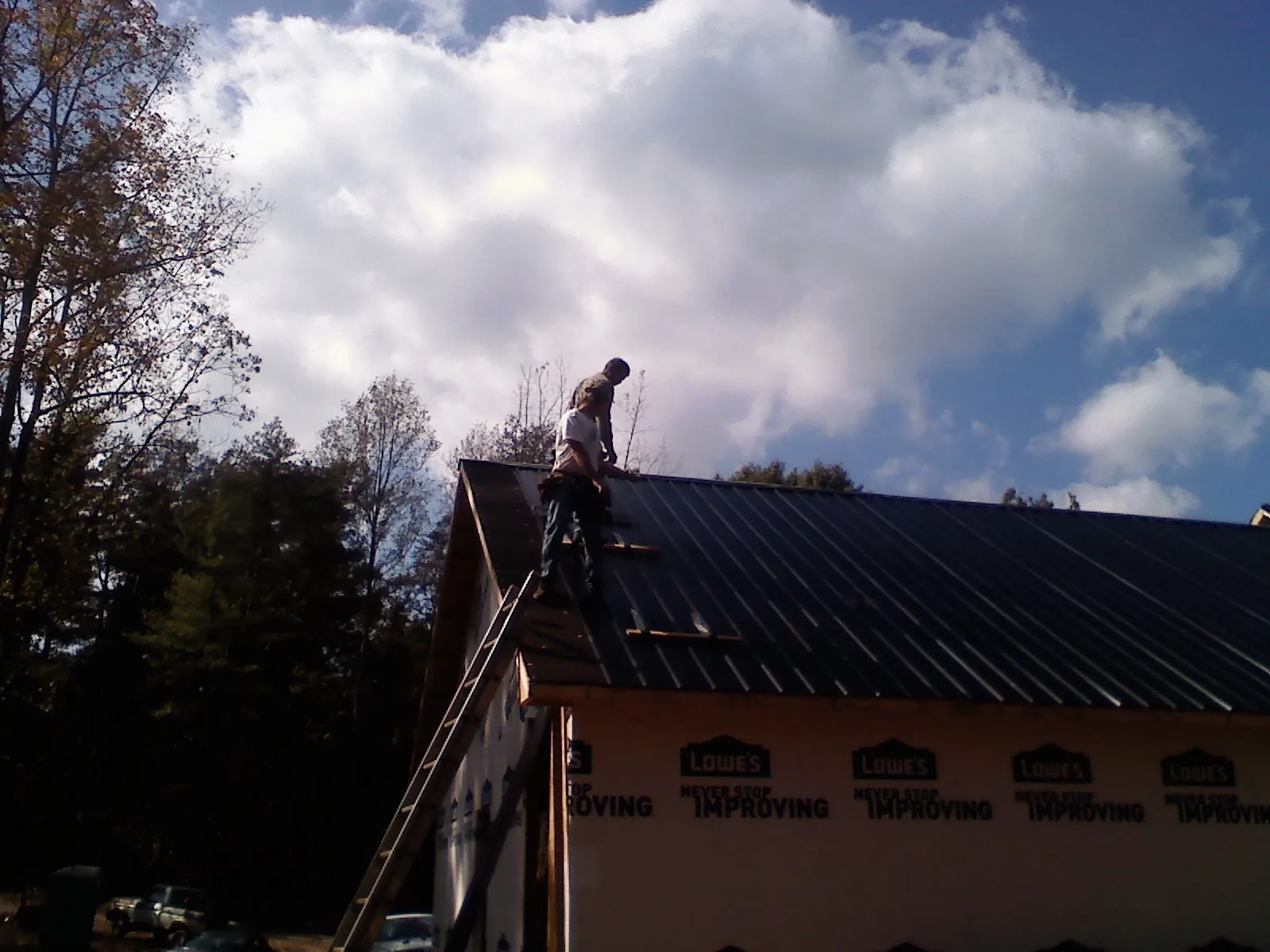Roofer fastening dark metal panels high against a cloudy sky, from a Roof Inspection job in Yoakum
